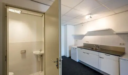 Keuken met witte kasten en een aangrenzende toiletruimte in een bedrijfsruimte aan de Hoogte Kadijk.